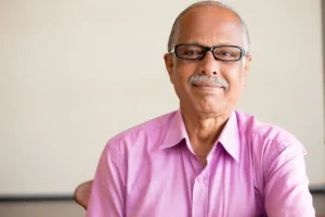 Elderly man in pink shirt and glasses smiling at the camera.