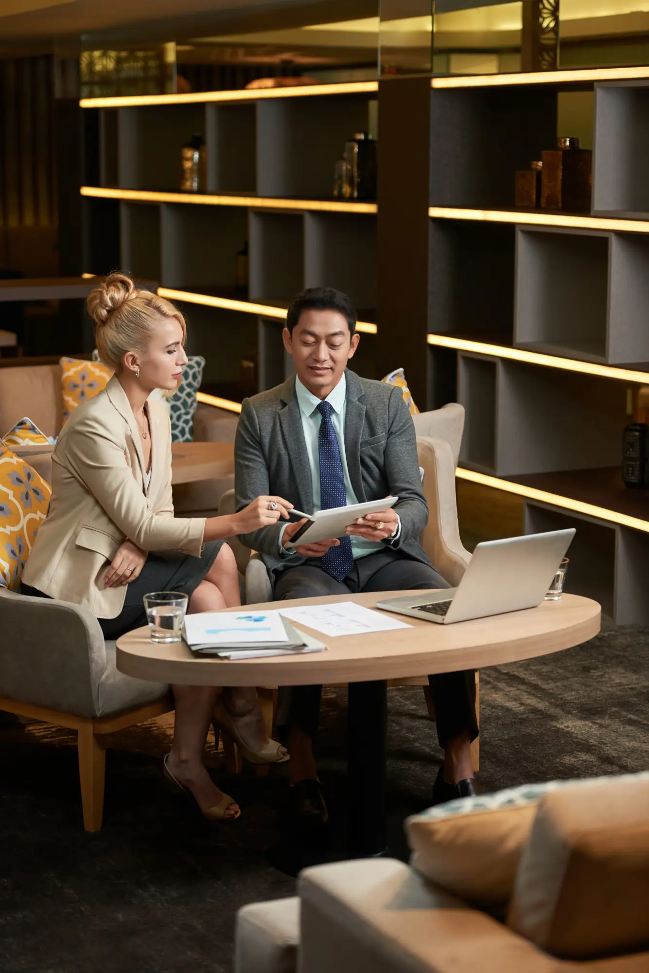 Businesswoman and businessman discussing documents together in a modern office lounge.