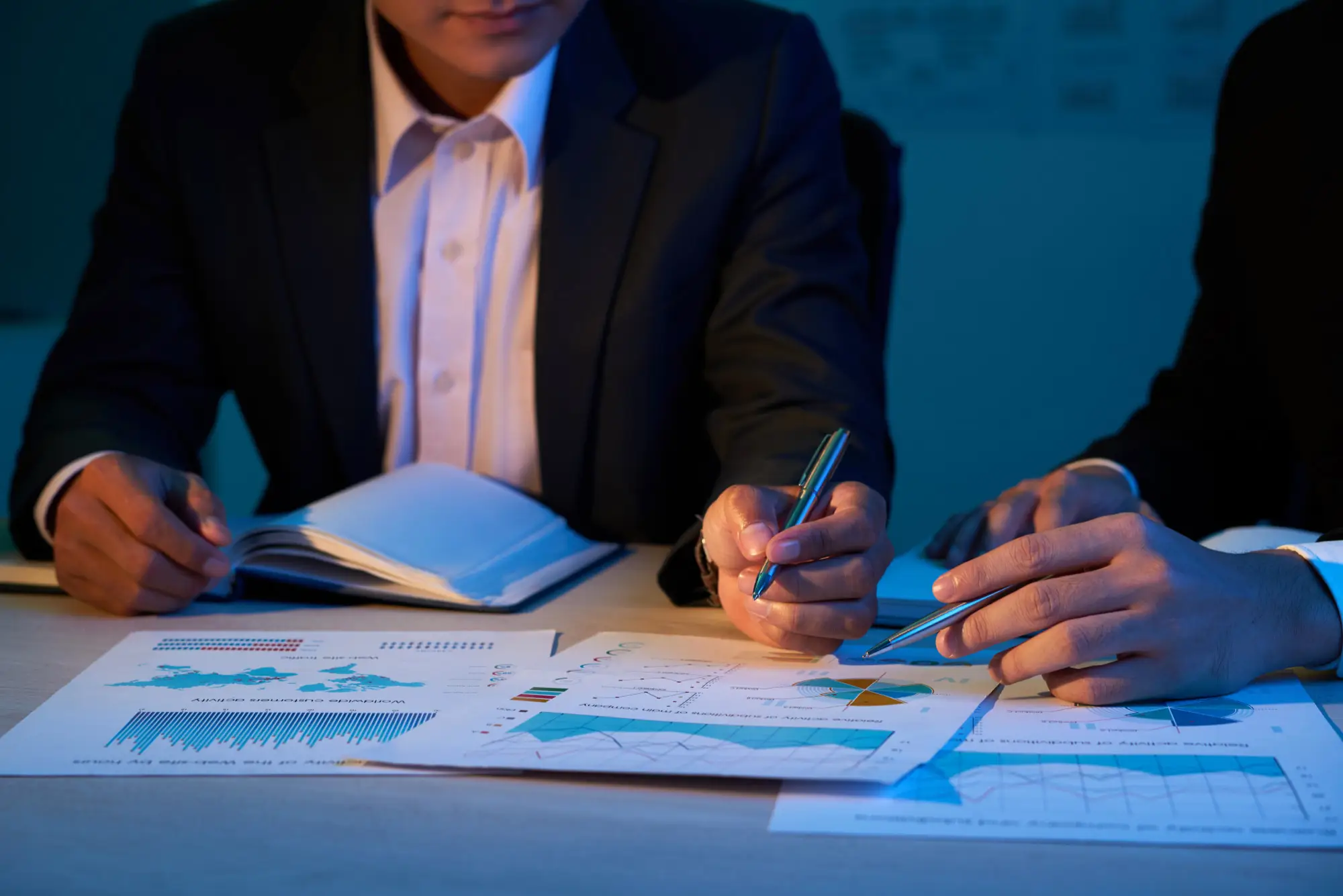 Businessmen reviewing financial charts and reports together with pens in hand.